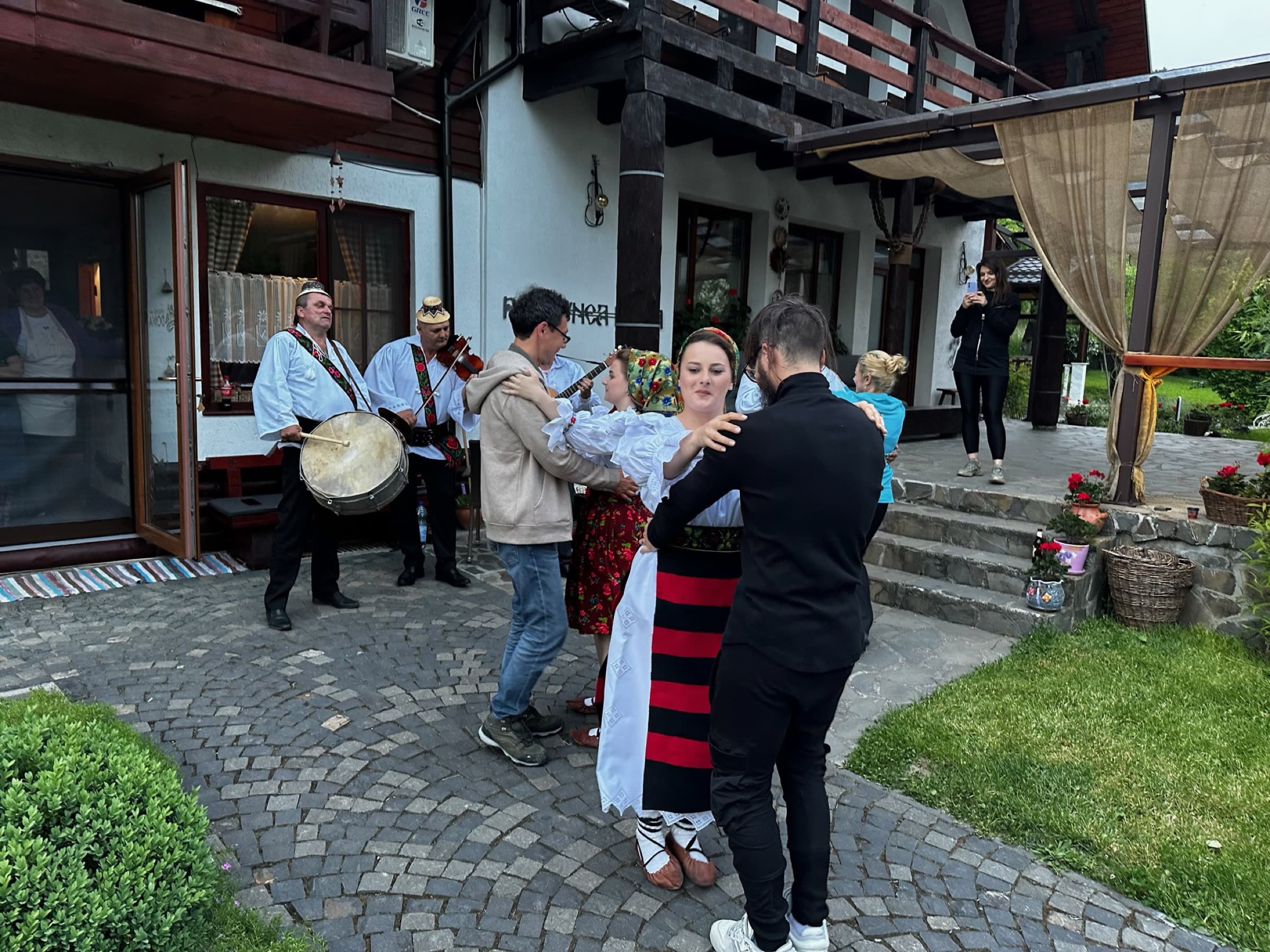 Ceterași cântând la vioară și dobă, cu oaspeți dansând în curte