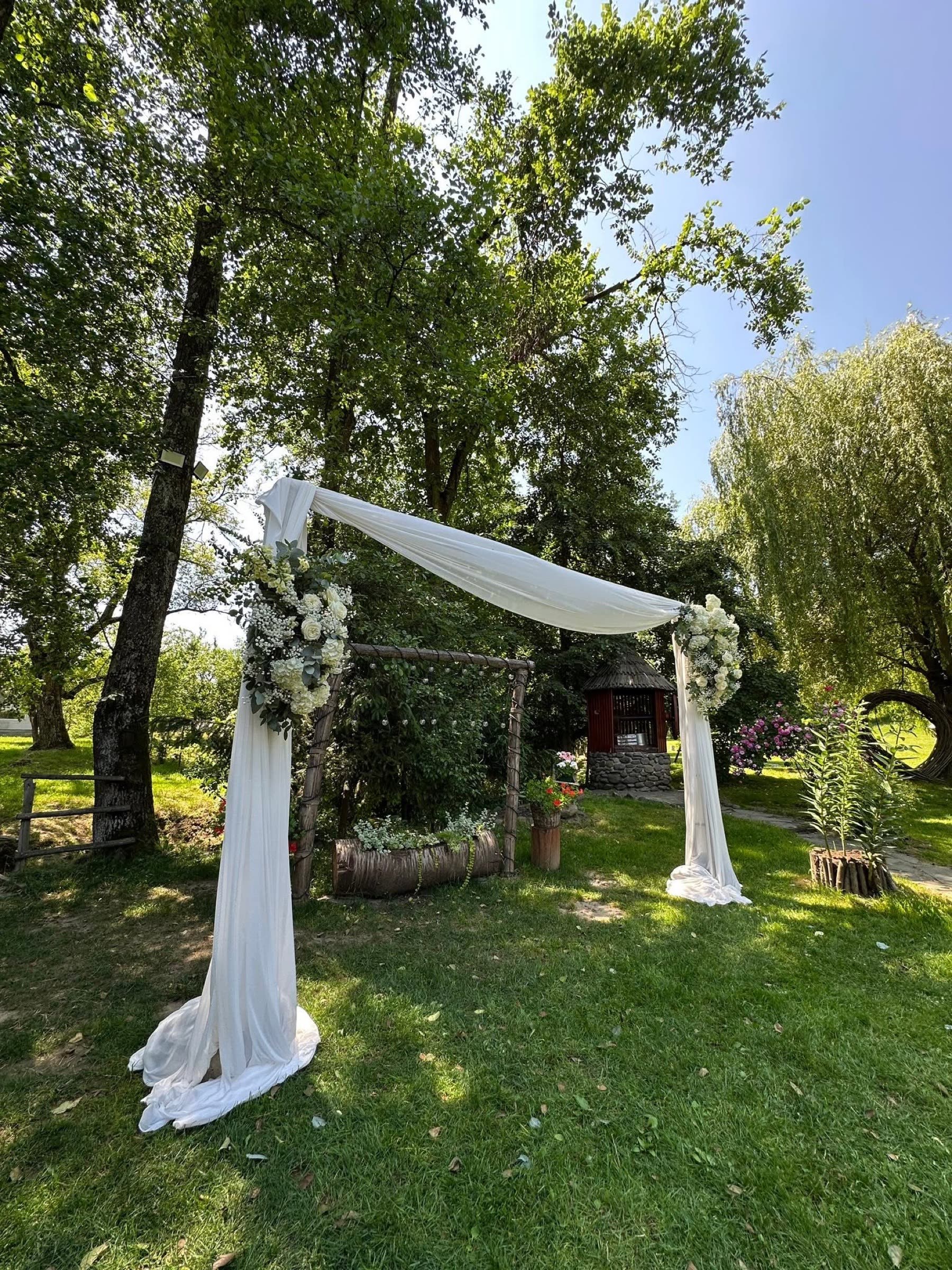 Arcadă de nuntă cu voal, pregătită pentru ceremonie în grădină