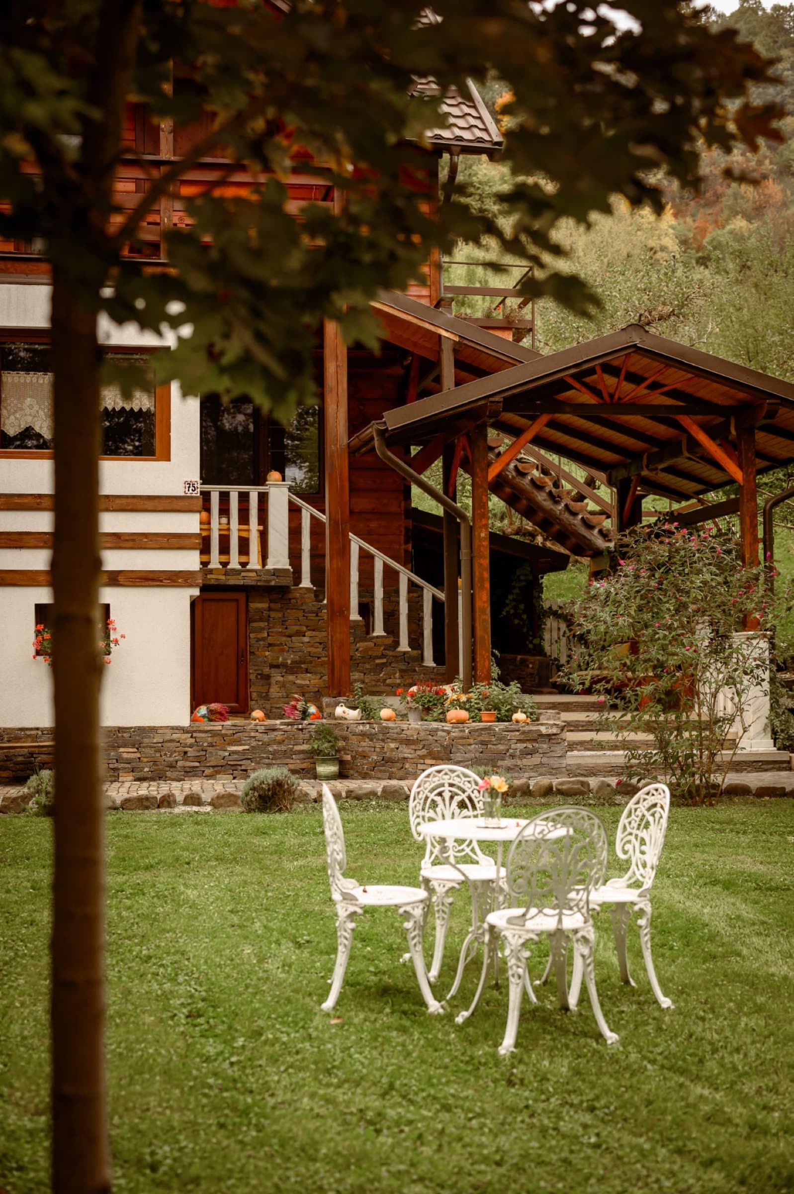 Masă albă de fier forjat pe iarbă, cu casa și foișorul în fundal