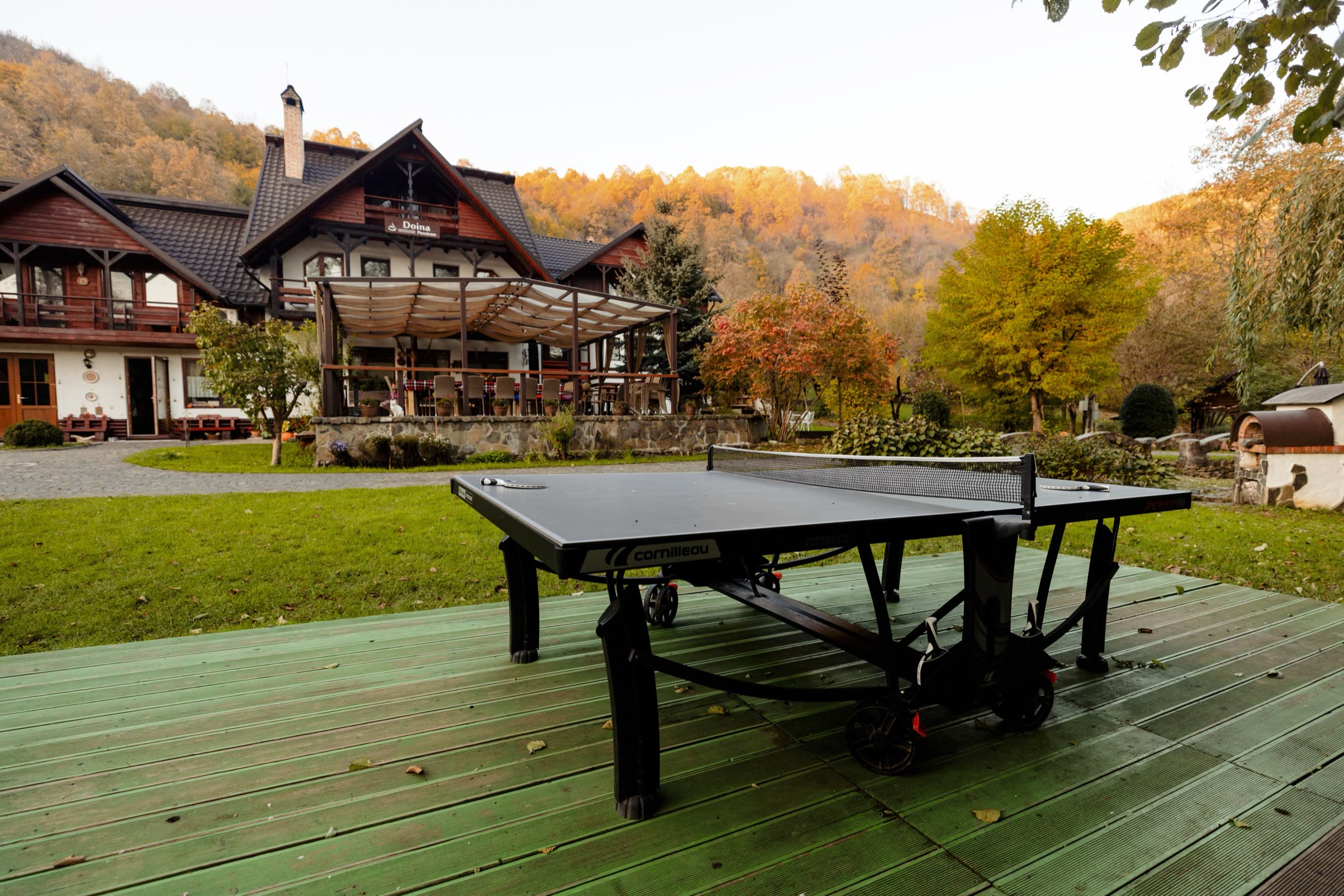 Masă de ping-pong pe terasa de lemn, cu dealul de toamnă în fundal